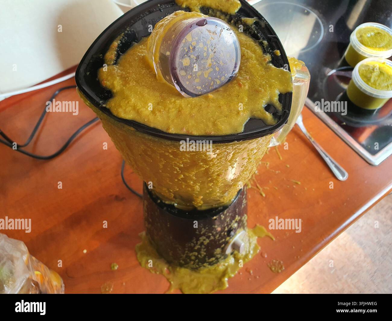 Un frullatore da cucina o un robot da cucina traboccante di una miscela densa, giallo-verde, che è fuoriuscita dal coperchio e colata lungo i lati del Foto Stock