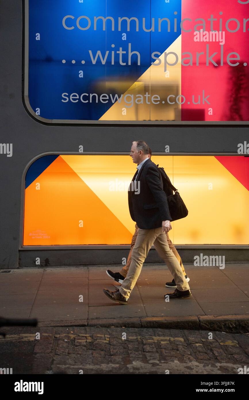I pedoni passano davanti all'ufficio illuminato di SecNewgate.co.uk su Greville Street a Londra durante il loro tragitto. Foto Stock