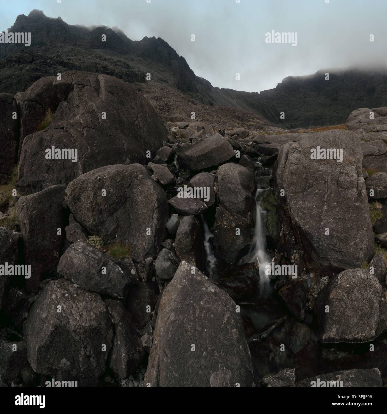Un torrente di montagna casca su massi sotto le aspre vette dei Cuillin sull'Isola di Skye, in Scozia. Foto Stock