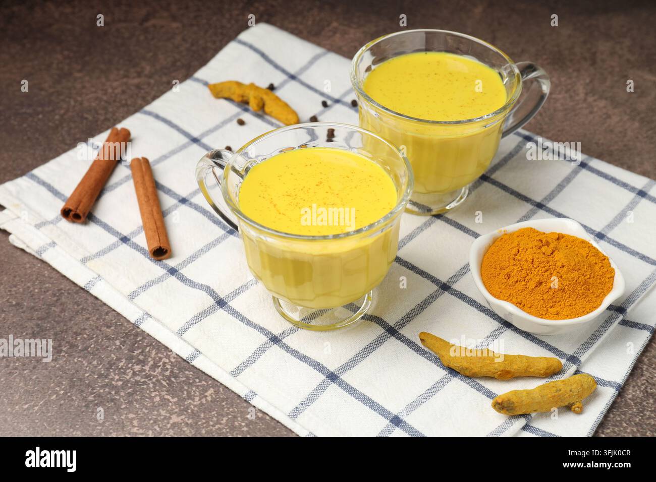 Latte dorato (latte al curcuma) in tazze e ingredienti su tavolo grigio, primo piano Foto Stock