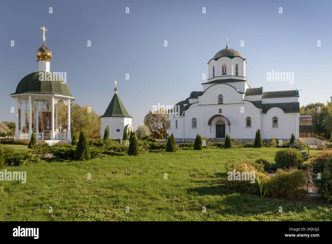 BARKOLABOVO, BIELORUSSIA – 8 OTTOBRE 2021: Vista panoramica di un complesso monastico ortodosso con una rotonda bianca e una chiesa dietro un aiuola autunnale.  Uno sp Foto Stock