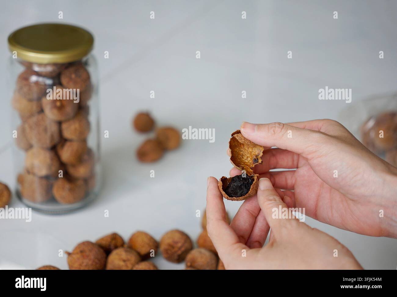 Mano tagliata che rompe un frutto di litchi essiccato Foto Stock