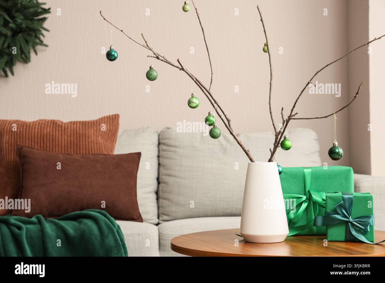 Decorazione natalizia e design di interni per le feste, rami minimalisti con ornamenti verdi e regali incartati su un tavolo di legno in un accogliente soggiorno Foto Stock