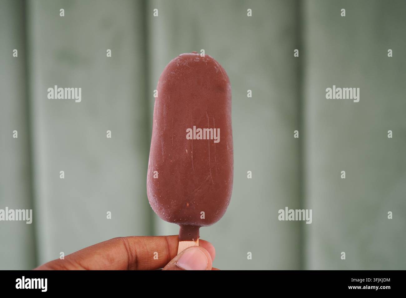 Popsicle di gelato al cioccolato tenuto in mano su uno sfondo verde Foto Stock