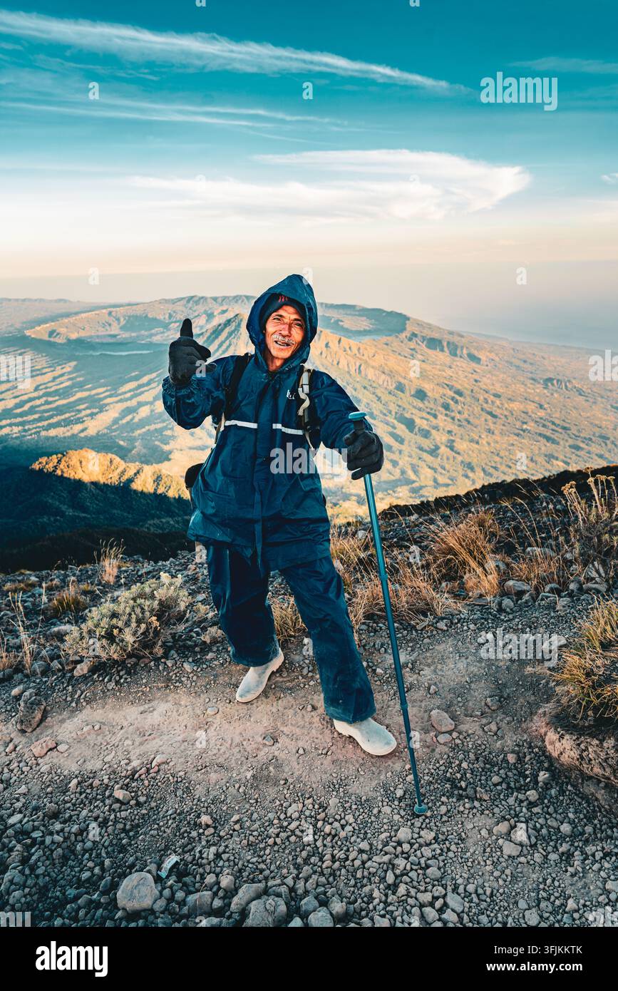 Una guida turistica esperta che posa per la fotocamera sulla cima del monte Agung con la caldera di Batur sullo sfondo. Foto Stock