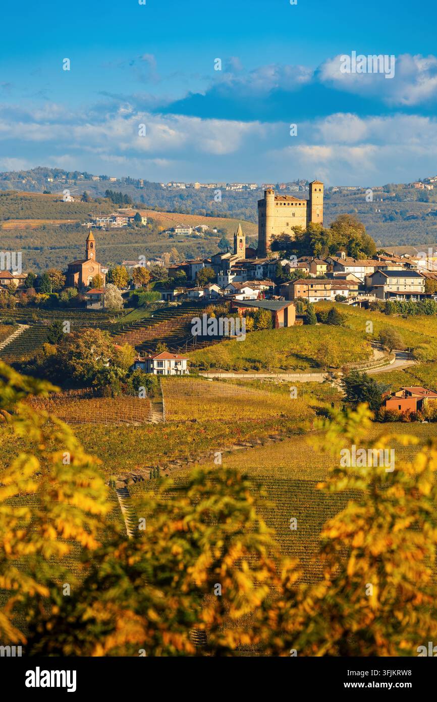 Paesaggio autunnale scenografico del villaggio medievale di Serralunga d'Alba con vigne dorate e colline ondulate sotto un cielo azzurro in Piemonte, Italia Foto Stock