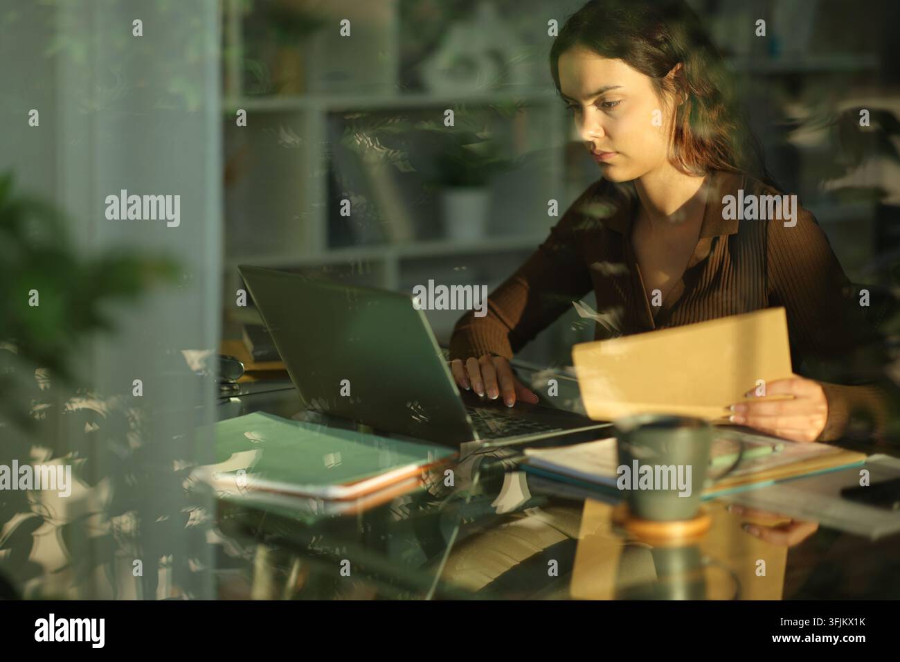 Teledipendente concentrato che lavora online, tiene documenti e controlla il laptop a casa Foto Stock