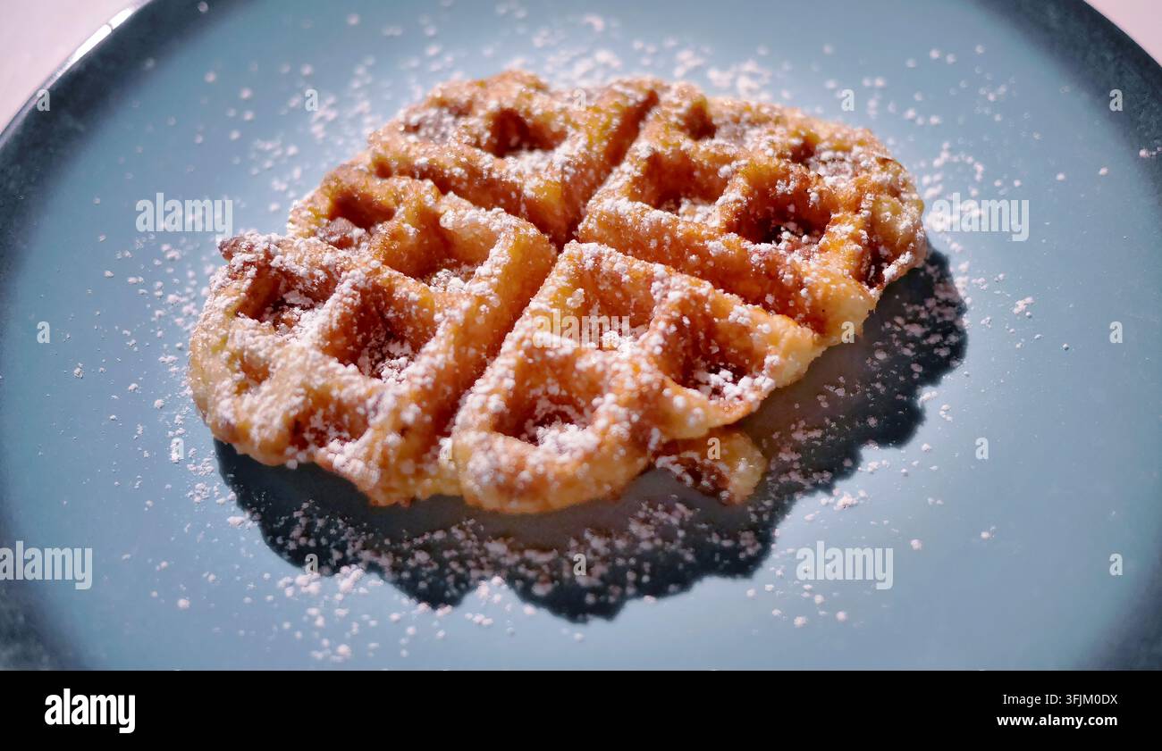 Fotografia stock di alta qualità di una waffle belga appena sfornata. Presenta una texture croccante dorata marrone ricoperta da una leggera spolverata di polvere bianca Su Foto Stock