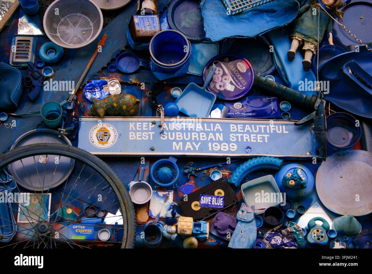 Opera d'assemblaggio colorata realizzata con oggetti blu attorno a un cartello centrale con la scritta “KEEP AUSTRALIA BEAUTIFUL BEST SUBURBAN STREET MAY 1989.” Foto Stock