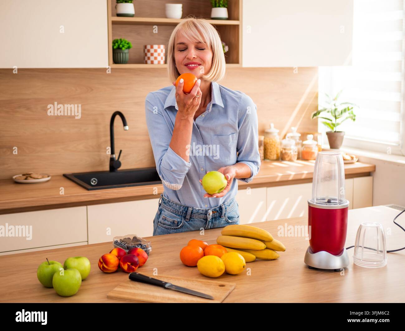 Concetto di alimentazione fresca e salutare con una donna circondata da frutta nutriente e attrezzature per preparare frullati. Foto Stock
