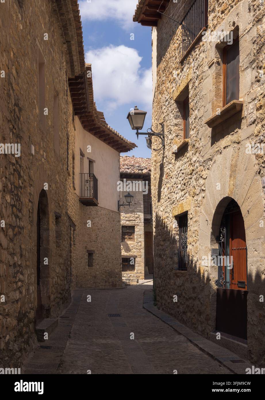 Una strada acciottolata si snoda attraverso la storica Mirambel, Teruel, con muri in pietra e un'atmosfera tranquilla. Foto Stock