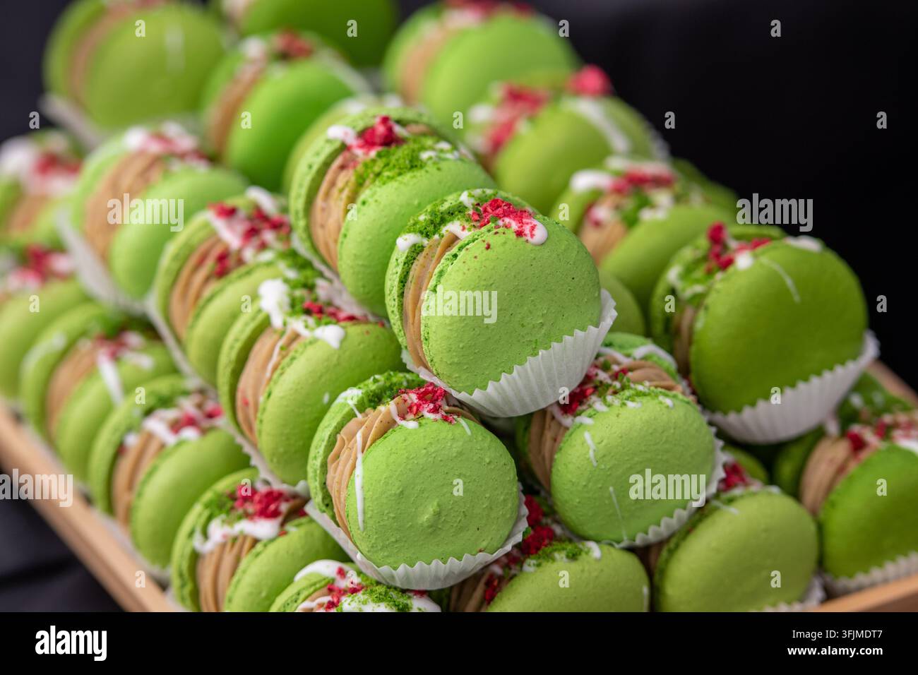Primo piano di macaron verdi al pistacchio ripieni di panna e decorati con frutti di bosco secchi e noci. Elegante dessert francese dai colori vivaci Foto Stock