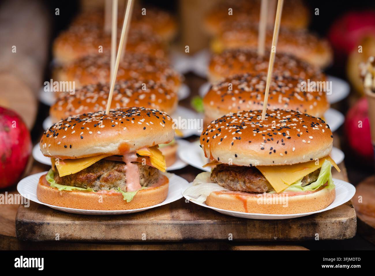 Hamburger serviti su piccoli piatti di carta disposti su una tavola di legno, guarniti con semi di sesamo e fissati con stuzzicadenti Foto Stock