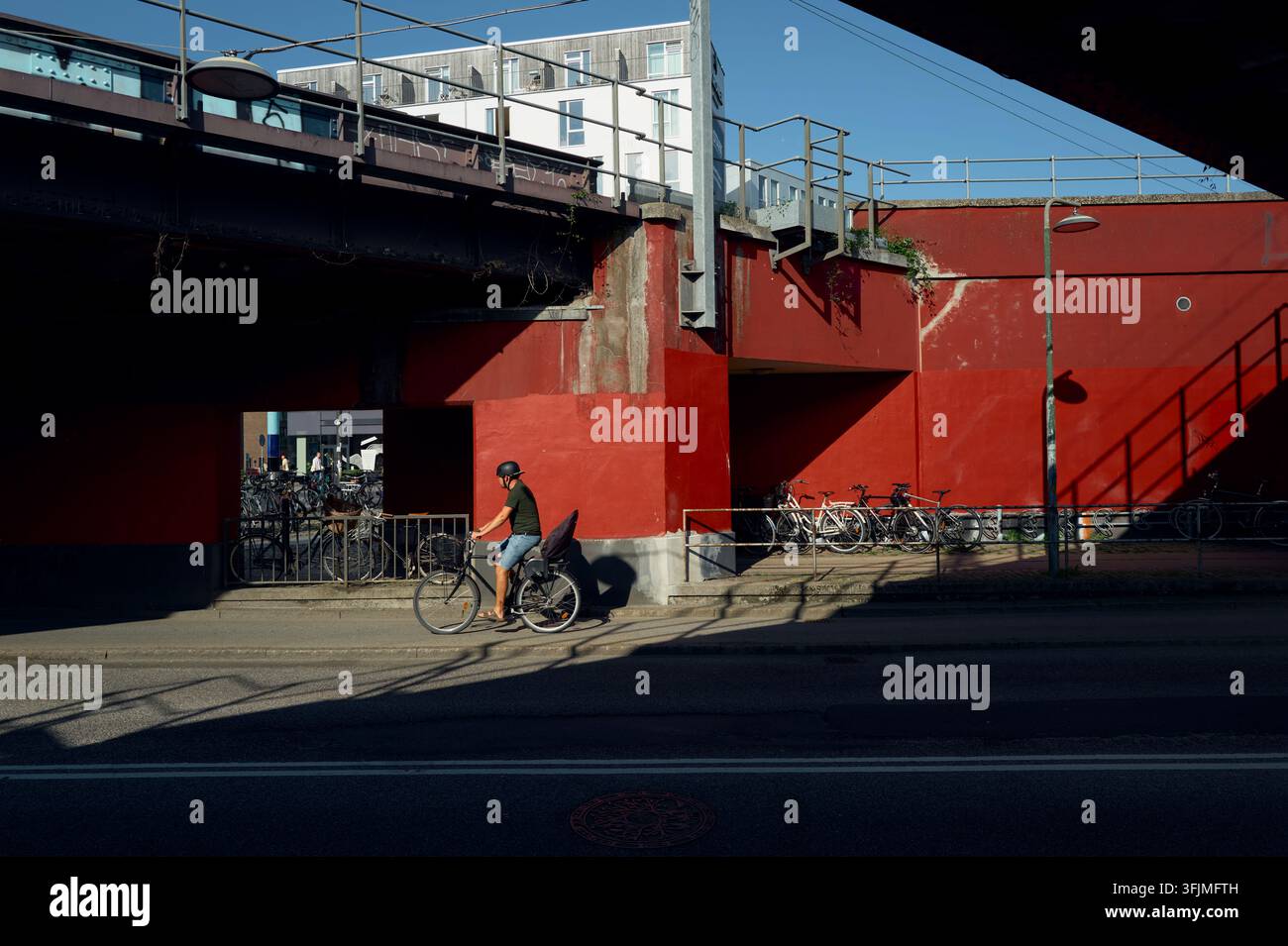 Uomo in bicicletta pedala al sole sotto un sottopassaggio rosso Foto Stock