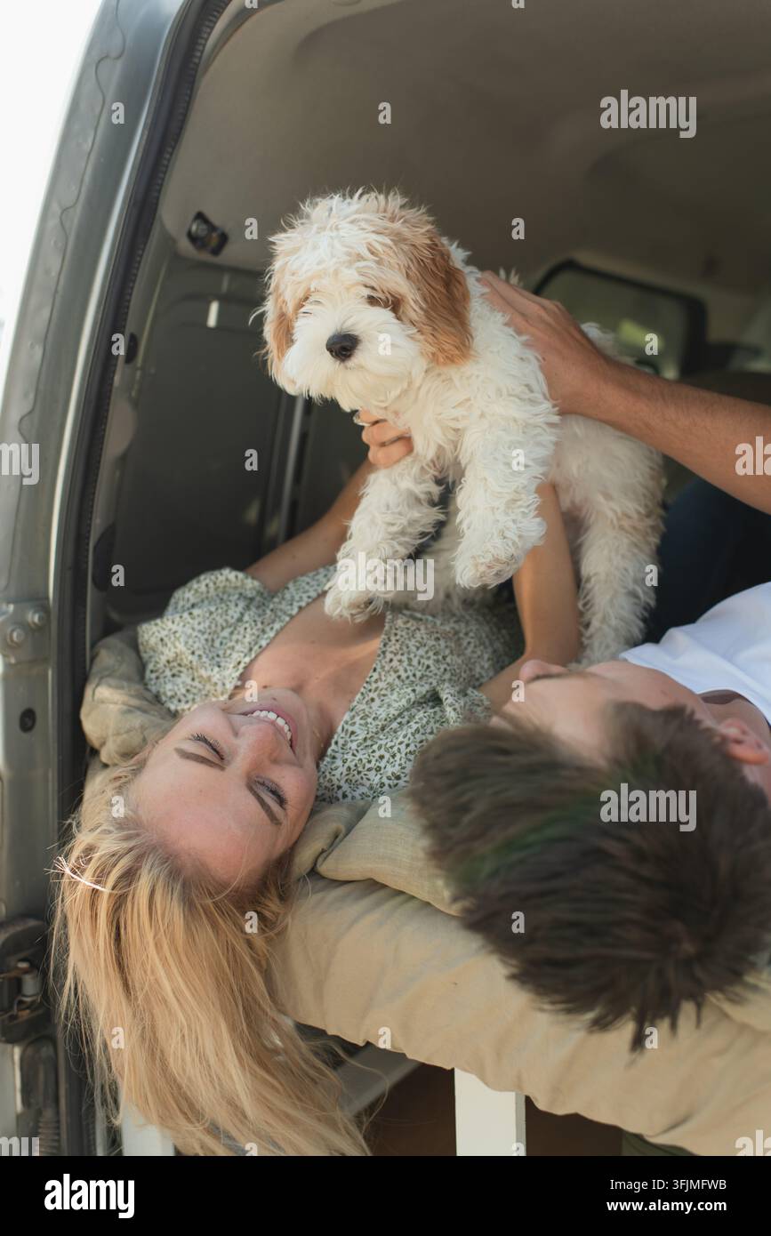 Giovane coppia felice che gioca con un cucciolo in un camper durante un viaggio Foto Stock