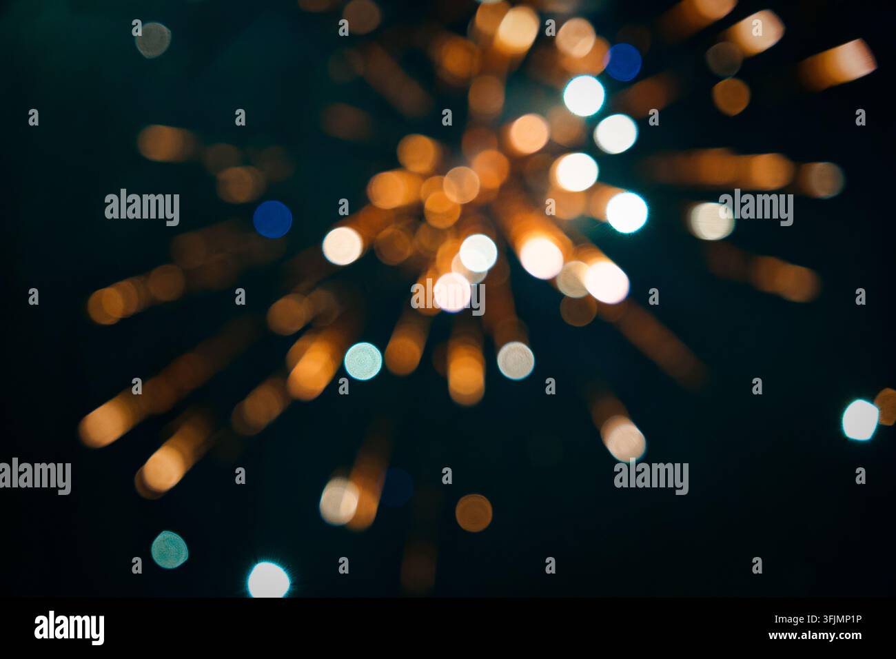Bokeh sfocato di fuochi d'artificio esplode in strisce radiali di arancione e blu contro un cielo notturno scuro, creando un motivo astratto onirico. Foto Stock