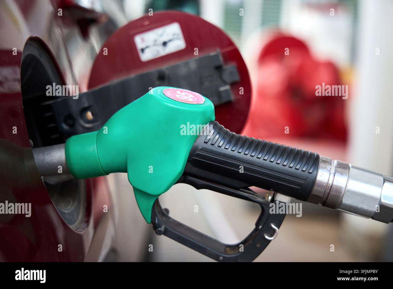 Ugello della pompa del carburante verde con etichetta di benzina senza piombo 95 che riempie il serbatoio di un'auto rossa alla stazione di servizio, vista ravvicinata durante il concetto di servizio auto Foto Stock