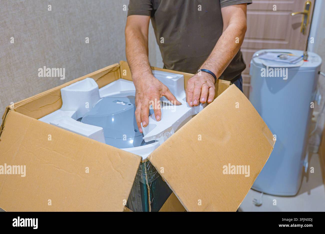 Idraulico che disimballa un nuovo scaldabagno nell'ambito di un progetto di sostituzione della caldaia elettrica Foto Stock