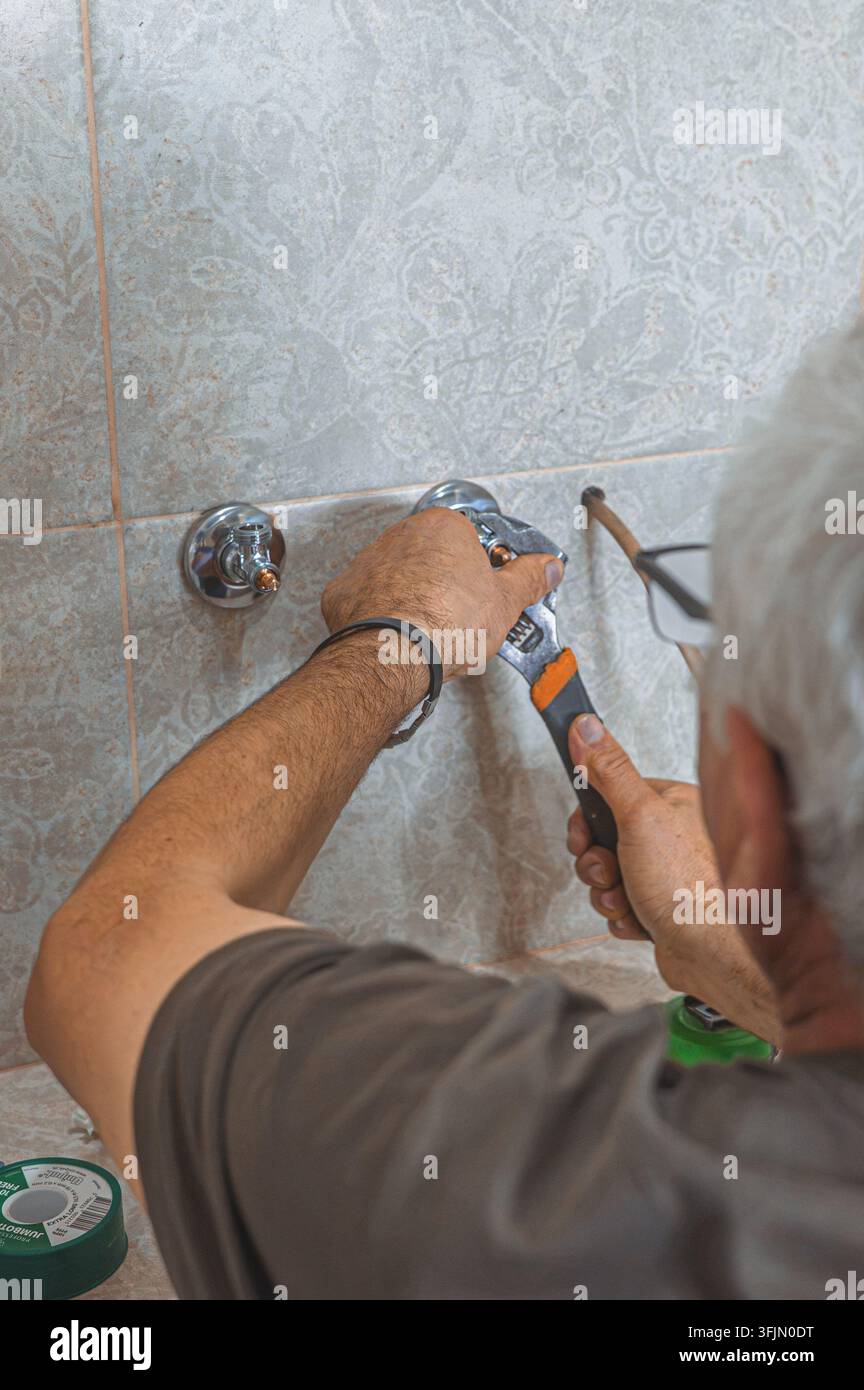 Idraulico che utilizza una chiave regolabile per collegare e stringere i tubi durante la caldaia domestica Foto Stock
