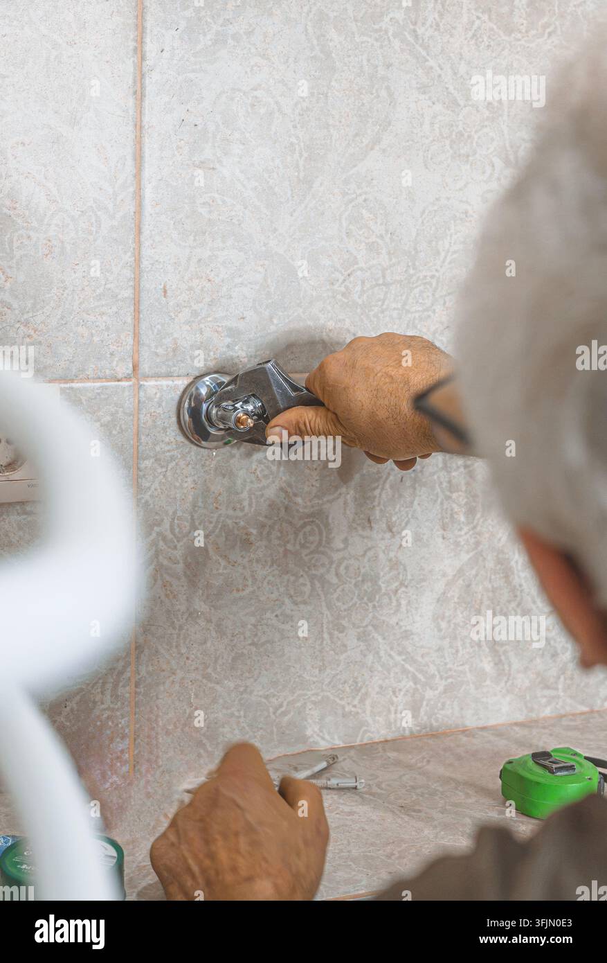 Idraulico che utilizza una chiave regolabile per stringere i collegamenti idraulici durante lo scaldabagno Foto Stock