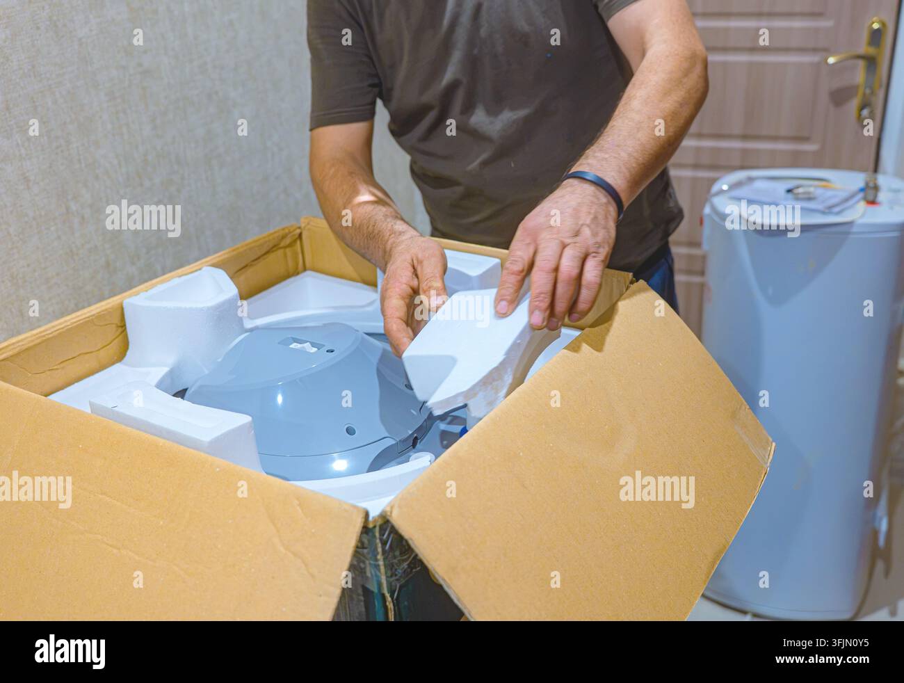 Idraulico professionista che disimballa un nuovo scaldabagno elettrico prima di sostituire una vecchia caldaia in un bagno di una casa residenziale. Riparazione e installazione di tubazioni Foto Stock