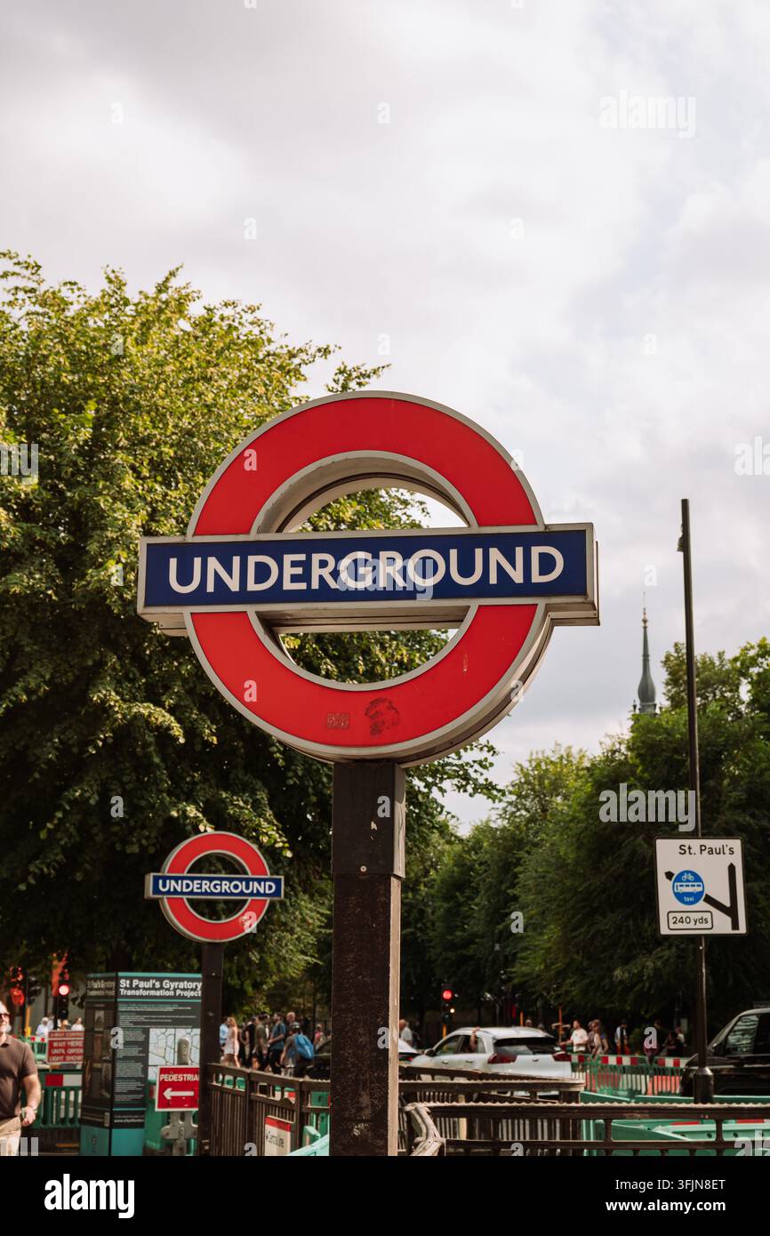 Londra, Inghilterra, Regno Unito, 15 agosto 2026. Primo piano di un'iconica insegna rotonda rossa e blu della metropolitana di Londra vicino alla stazione di St Paul con alberi Foto Stock