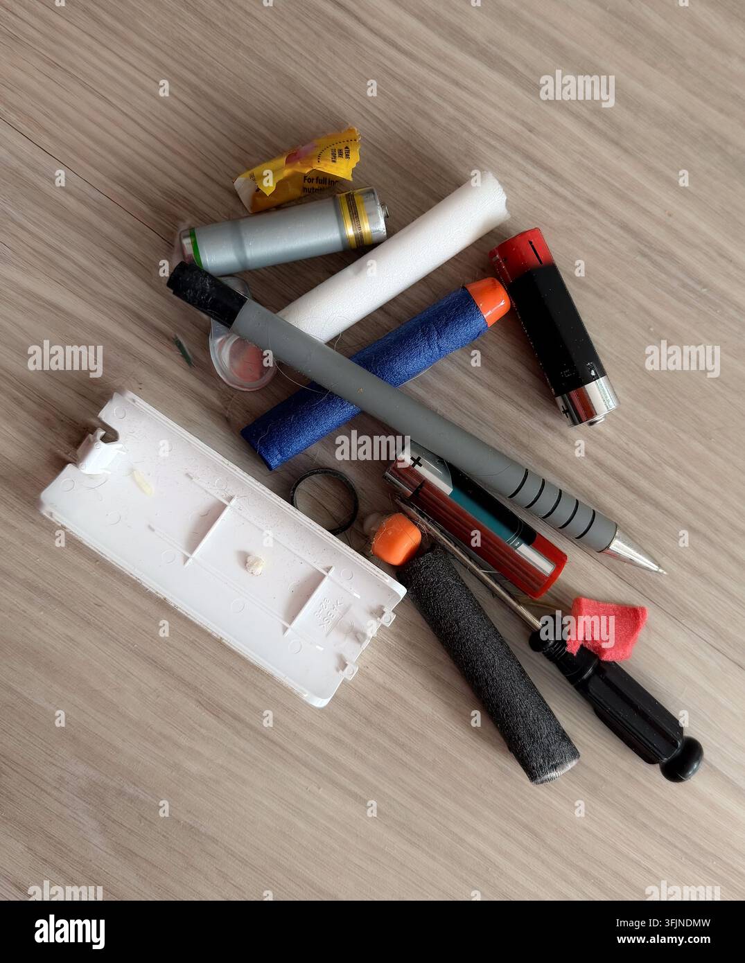 Un mucchio di piccoli rifiuti domestici, batterie AA, frecce giocattolo in schiuma, una penna meccanica e detriti raccolti da sotto un cuscino del divano su pavimento di legno. Foto Stock