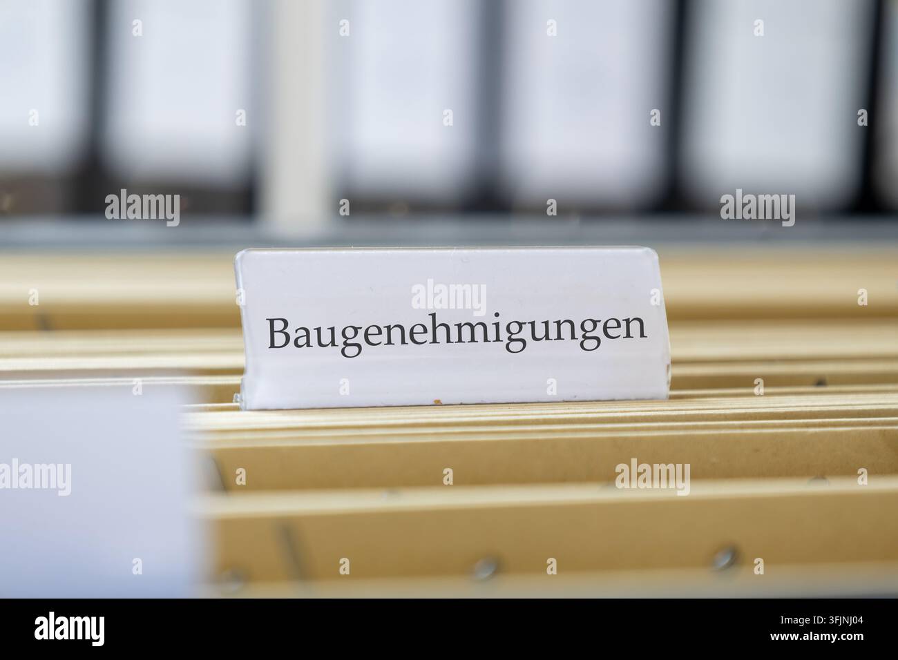 (Fotomontaggio) Cartello con le parole BAUGENEHMIGUNGEN (permessi di costruzione) su uno scaffale per documenti sospeso Foto Stock