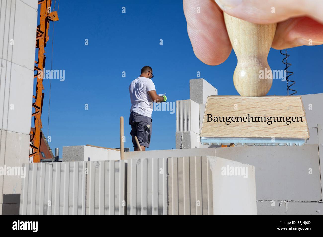 (Fotomontaggio) Un francobollo con le parole BAUGENEHMIGUNGEN (permessi di costruzione) davanti a un cantiere edile Foto Stock