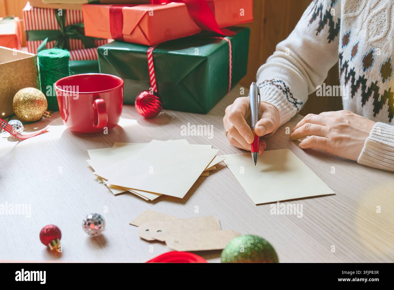 Donna che scrive biglietti di Natale ed etichette per i regali a casa. Prepara messaggi festivi personalizzati ed etichette per i regali, illustrando idee regalo stagionali Foto Stock