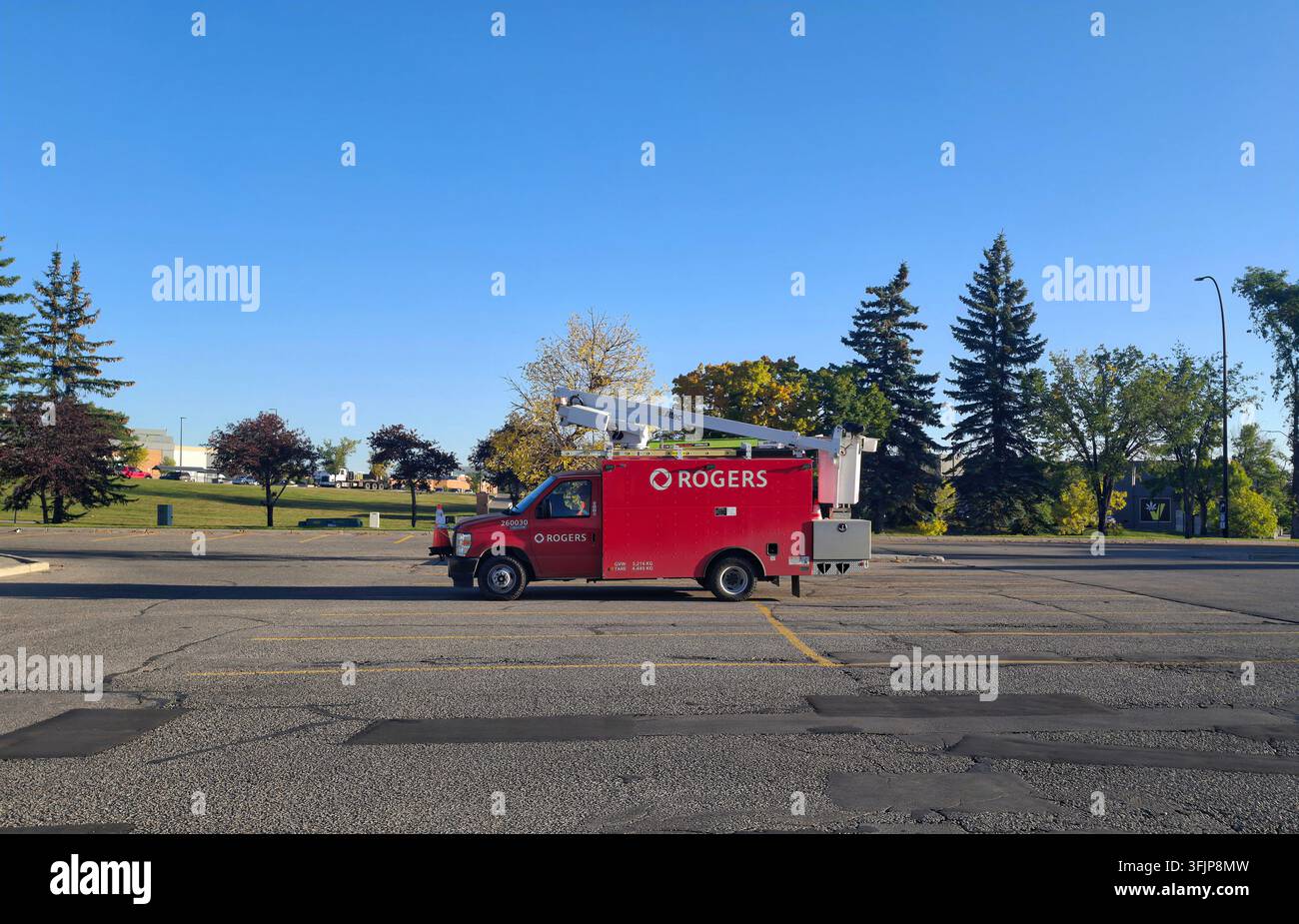 CALGARY, CANADA - 18 SETTEMBRE 2026: Un furgone di servizio Rogers Communications rosso acceso equipaggiato con un cestino elevatore telescopico parcheggiato o Foto Stock