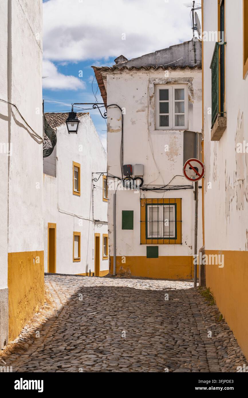 Vista di una stretta strada acciottolata fiancheggiata da edifici tradizionali imbiancati a calce con decorazioni gialle e lanterne in ferro battuto nel centro storico Foto Stock