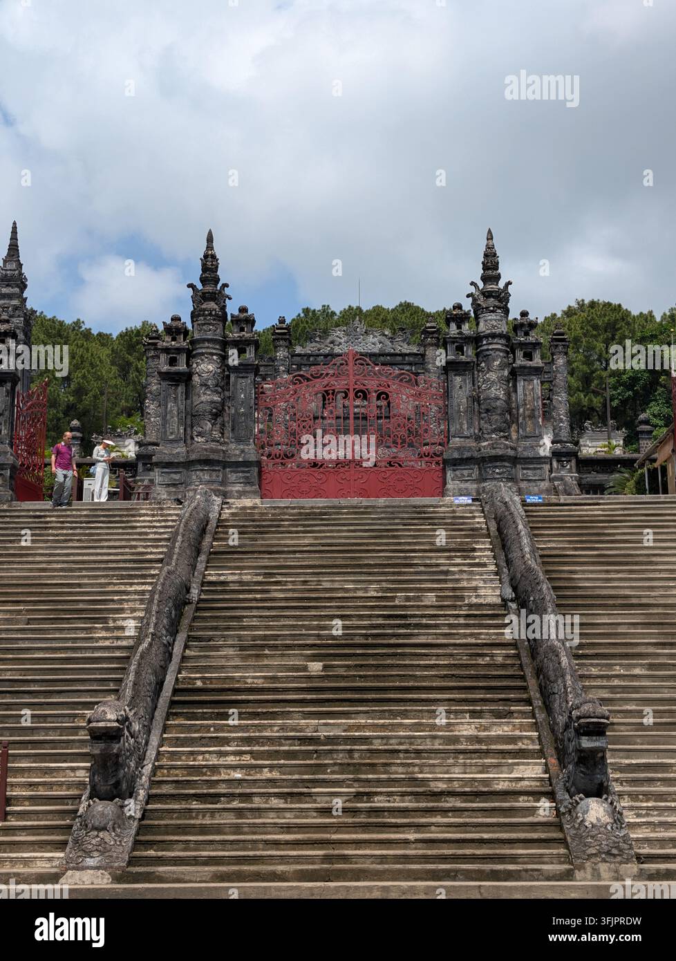 HUE, VIETNAM - 15 MARZO 2026: Grande scalinata in pietra fiancheggiata da balaustre a forma di drago che conduce a un cancello rosso ornato al tomba storica di Khai Dinh - Immagine stock catturata con smartphone