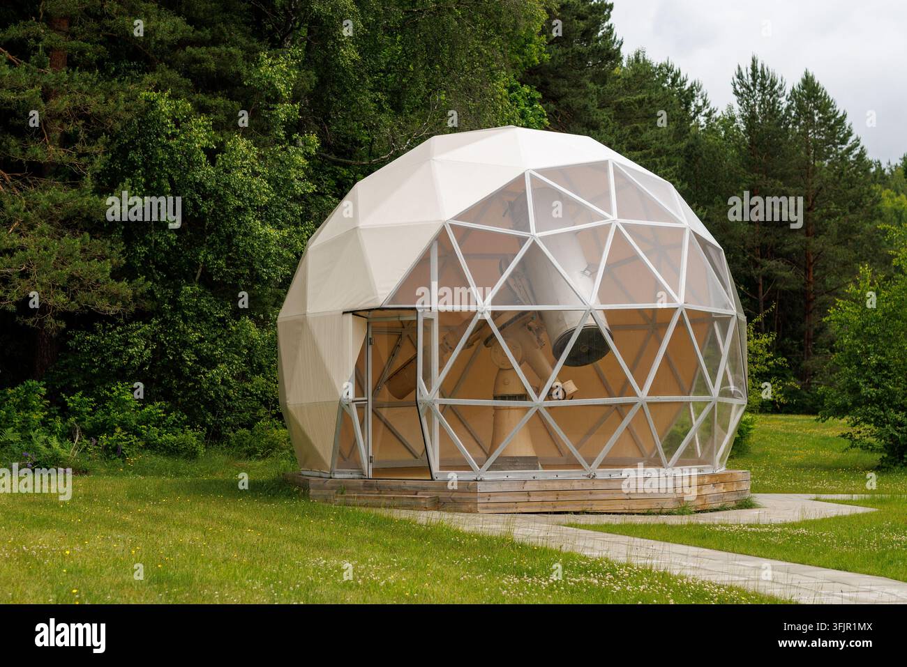 Un osservatorio telescopio a cupola geodetica bianca in piedi su un campo erboso circondato da alberi verdi. I pannelli anteriori trasparenti rivelano la sci interna Foto Stock