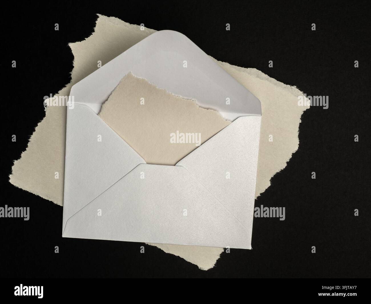 Una busta bianca aperta che contiene un foglio di carta strappato su uno sfondo nero, che suggerisce posta, cartoleria, corrispondenza, inviti, messaggi, minimalismo Foto Stock