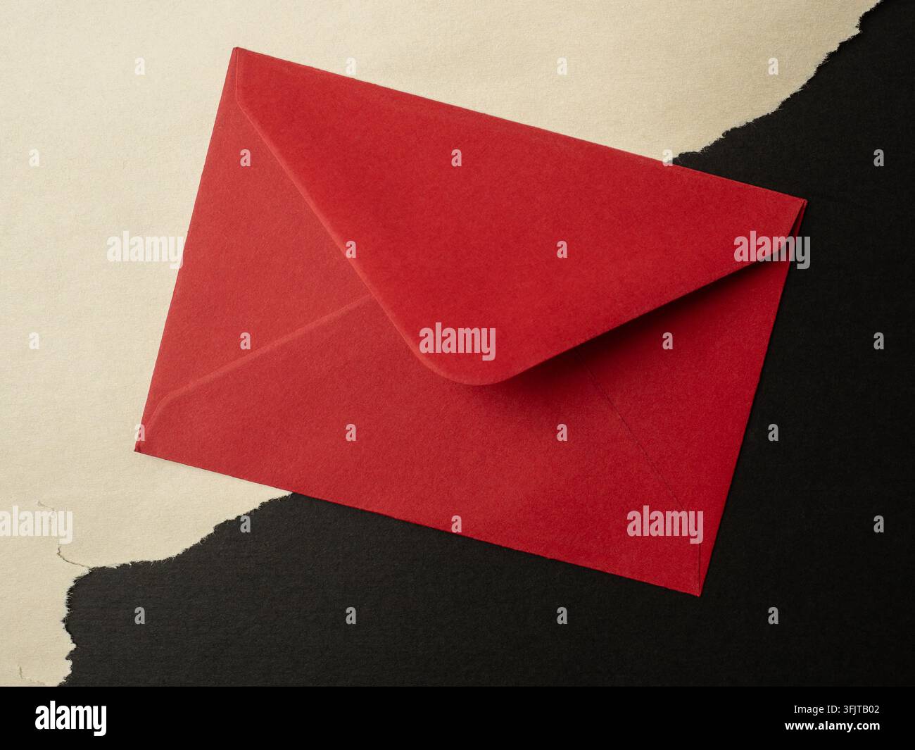 Una busta rossa giace su carta nera e crema strappata, suggerendo inviti, note di San Valentino, messaggi segreti, regali e corrispondenza romantica in una mi Foto Stock