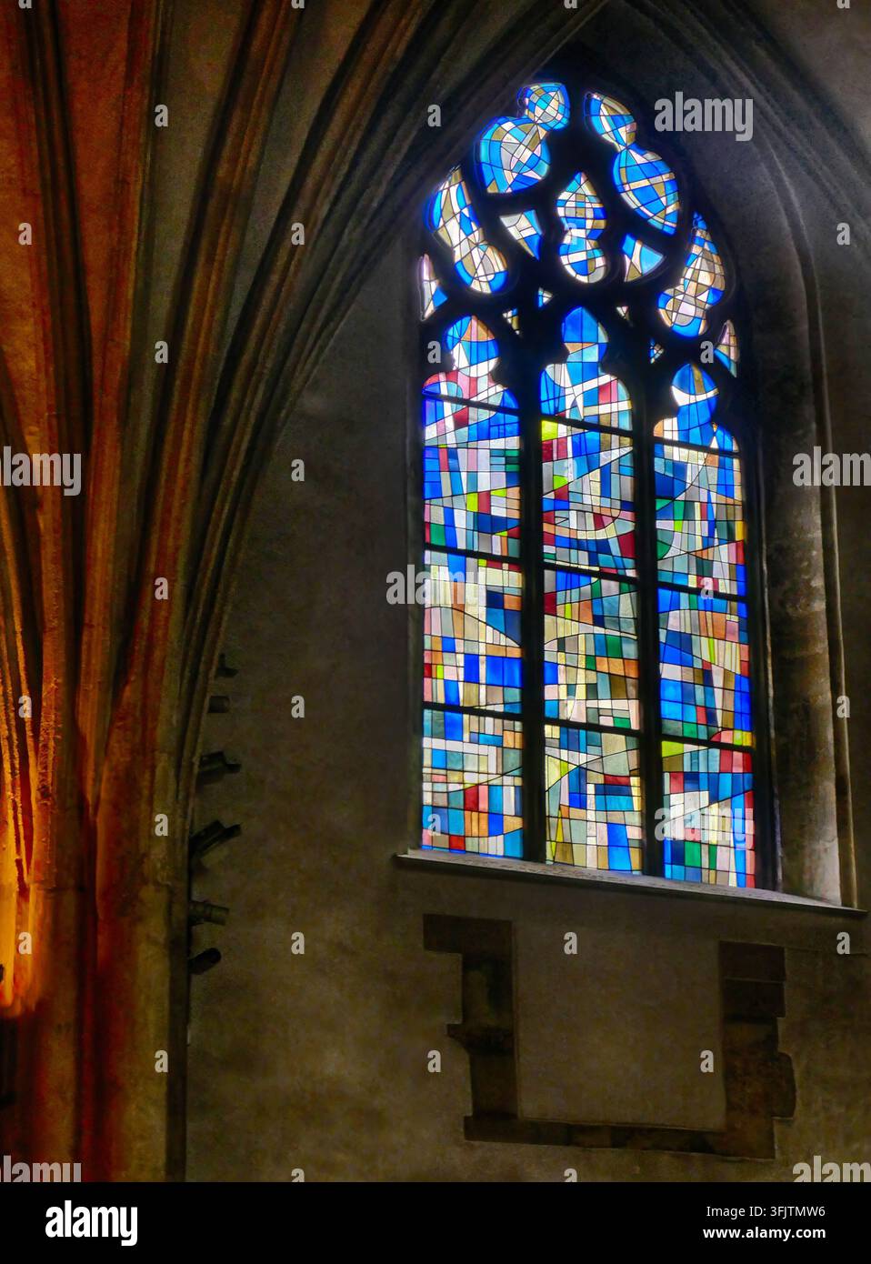 Interno della chiesa che mostra l'imponente finestra gotica ad arco con vetrate di design astratto contemporaneo che illuminano brillantemente l'arco storico Foto Stock