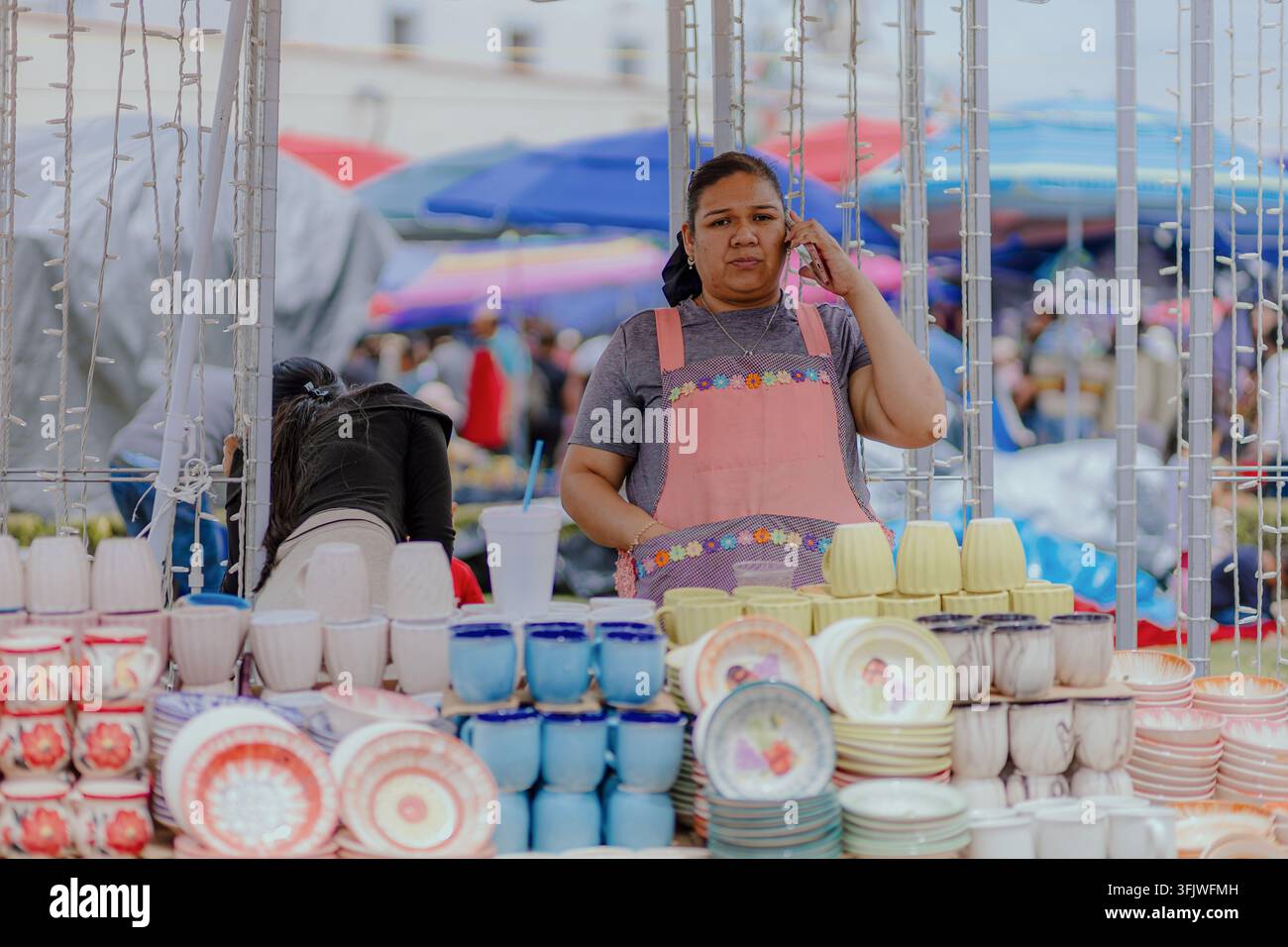 San Pedro Cholula, Messico - 8 settembre 2026: Una donna si trova dietro una vetrina di tazze e piatti in ceramica alla fiera tradizionale del baratto Trueque. Foto Stock