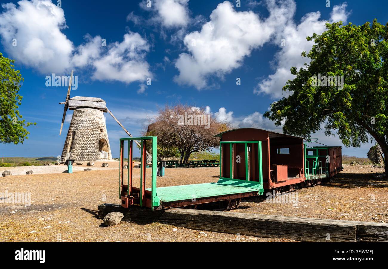 Antico mulino a vento in pietra e vecchio carro per il trasporto della canna da zucchero sulla piantagione di Betty's Hope sotto un cielo azzurro ad Antigua e Barbuda. Foto Stock