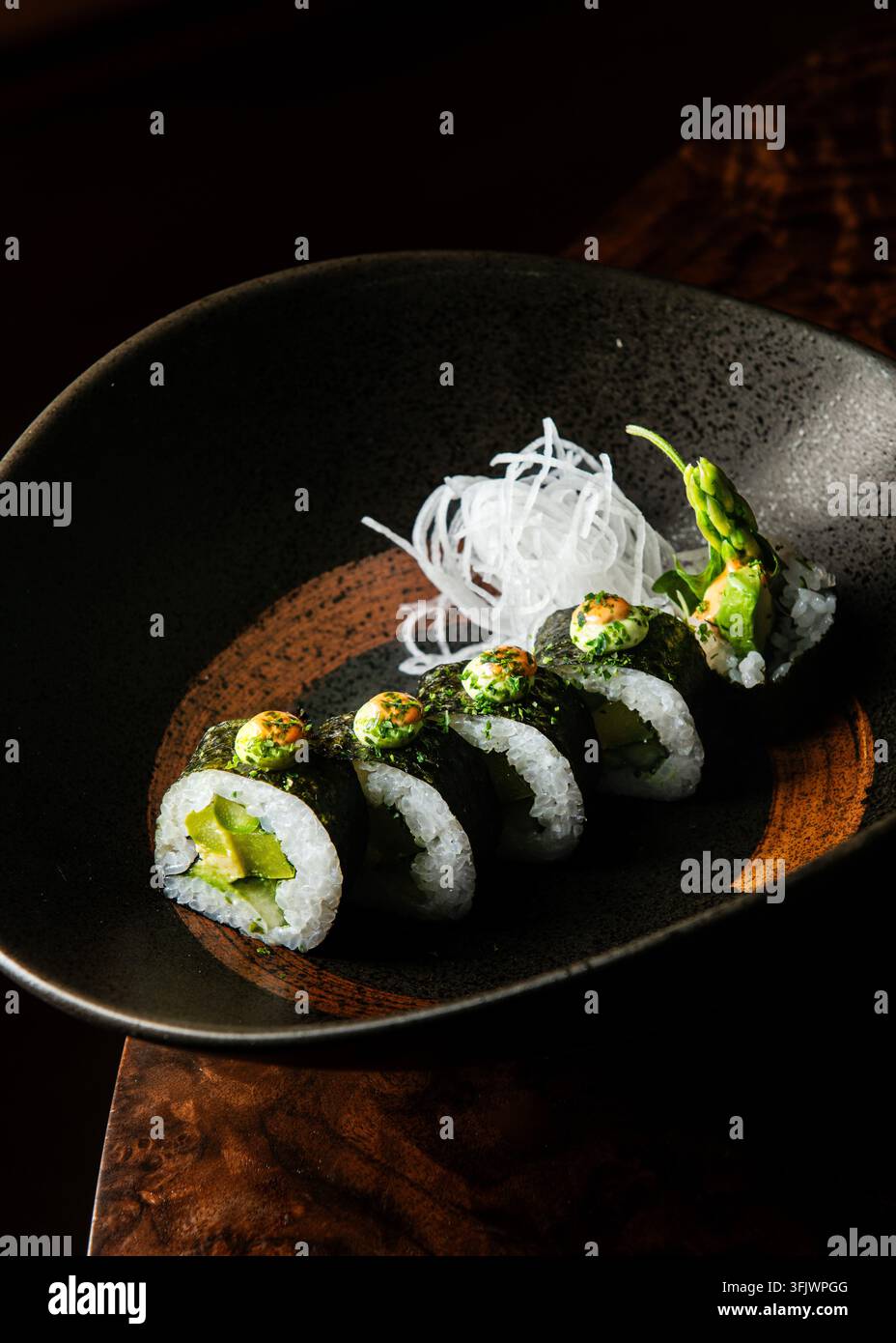 Vista laterale foto professionale di rotoli di sushi vegetali gourmet ripieni di asparagi e avocado, guarniti con salsa verde e ravanello daikon in Foto Stock