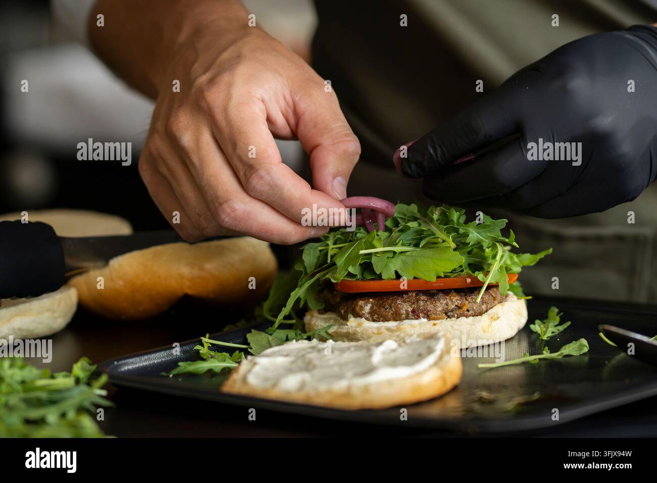Hamburger di manzo assemblato appena con una succosa polpetta di manzo, rucola croccante, fette di pomodoro e cipolla rossa sottaceto su un panino morbido. Foto Stock