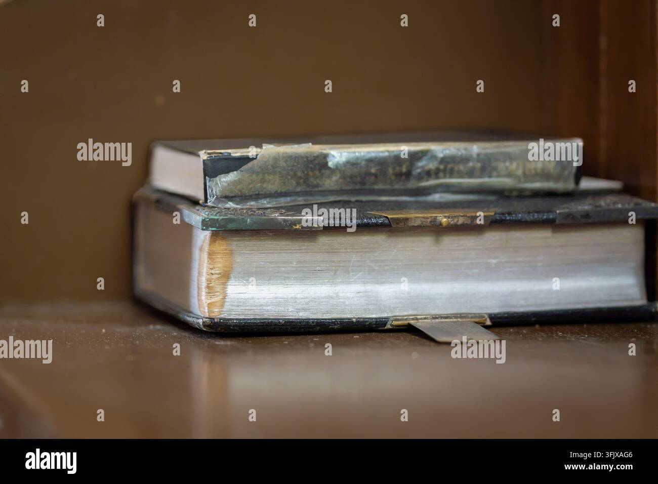 Una vecchia Bibbia appoggiata su un banco di chiesa in legno consumato, il suo rivestimento in pelle invecchiata, le pagine consumate e la rilegatura tradizionale rivelano anni di utilizzo. Foto Stock