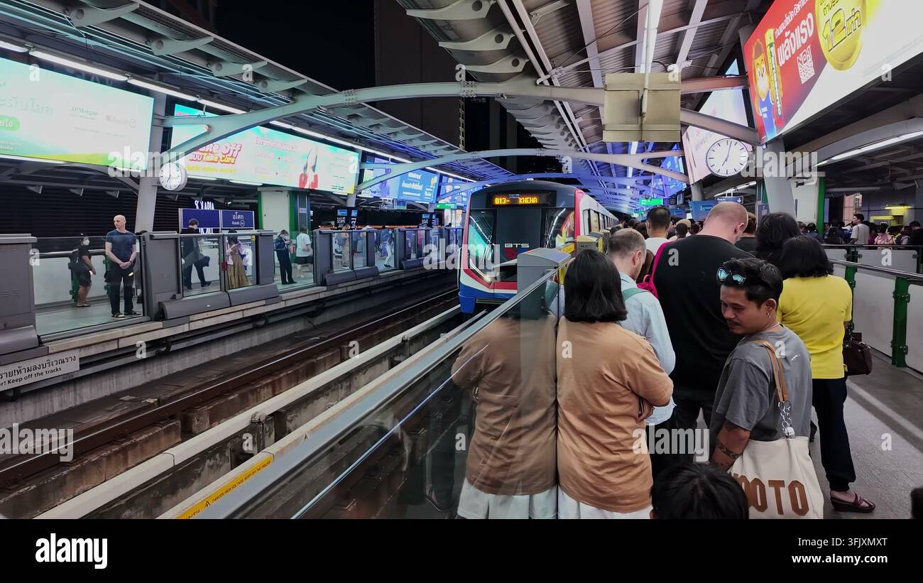 BANGKOK, THAILANDIA - 27 GEN 2025: Passeggeri in attesa sul binario della stazione Asok BTS Skytrain mentre arriva un treno di transito rapido durante le ore serali Foto Stock