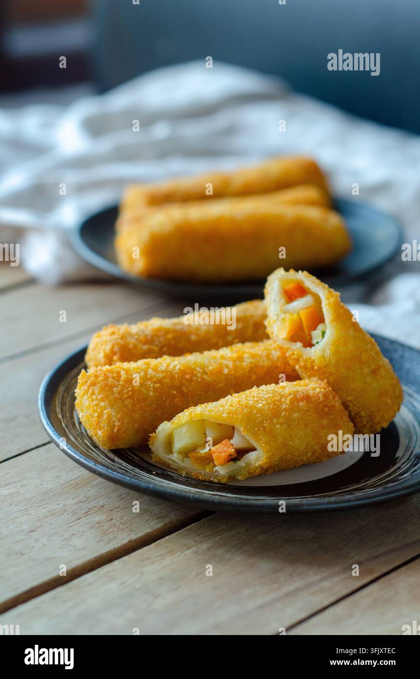 Risoles indonesiani, snack fritti panati croccanti serviti su piatti neri su un tavolo di legno, con uno tagliato aperto per mostrare il ripieno. Foto Stock