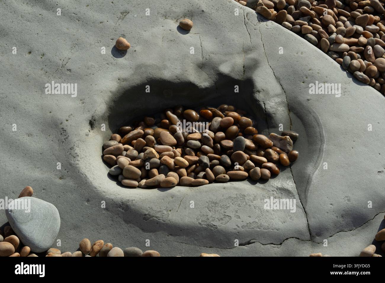 Maree e onde raccolgono ciottoli marroni lisci in una cavità rocciosa erosa a Seatown Beach sulla costa giurassica del Dorset, Regno Unito. Foto Stock