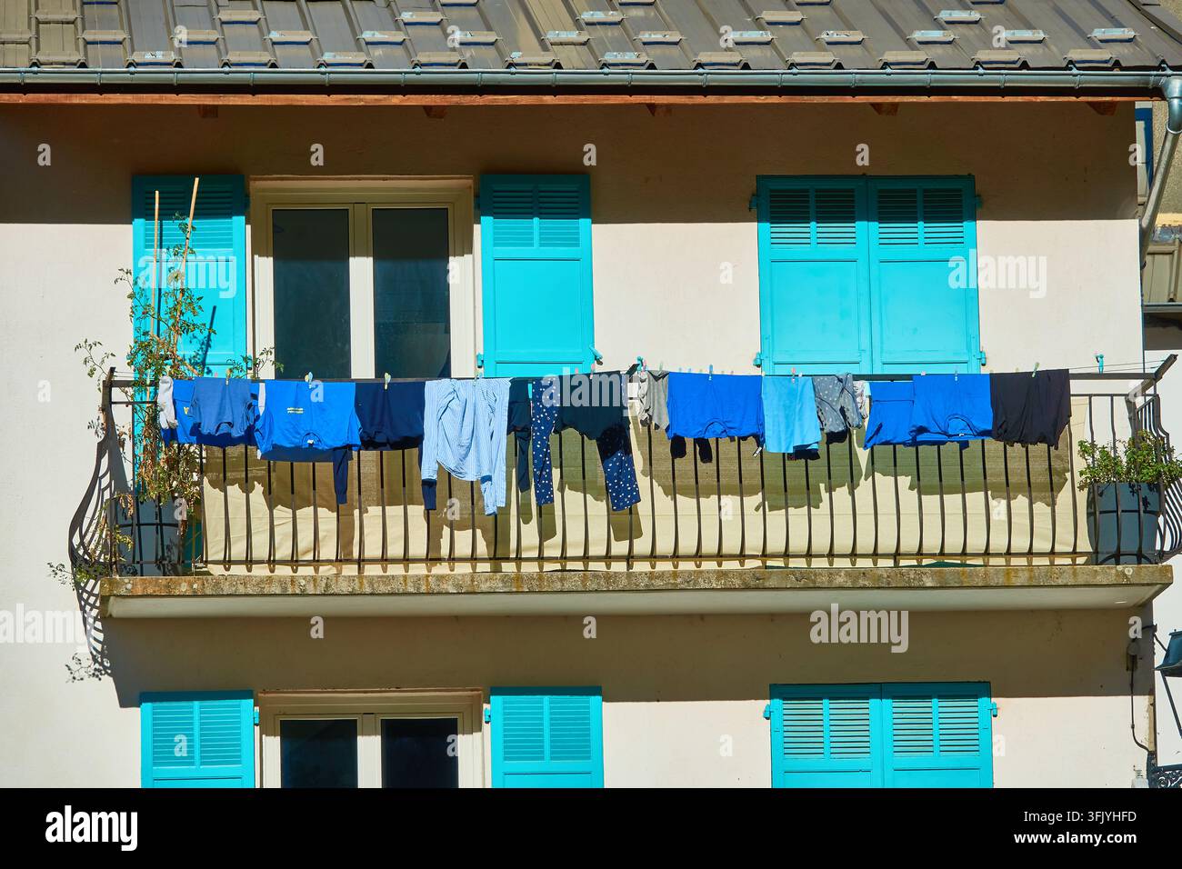 Biancheria da balcone illuminata dal sole con vestiti blu appesi a una corda da bucato sotto persiane turchesi Foto Stock