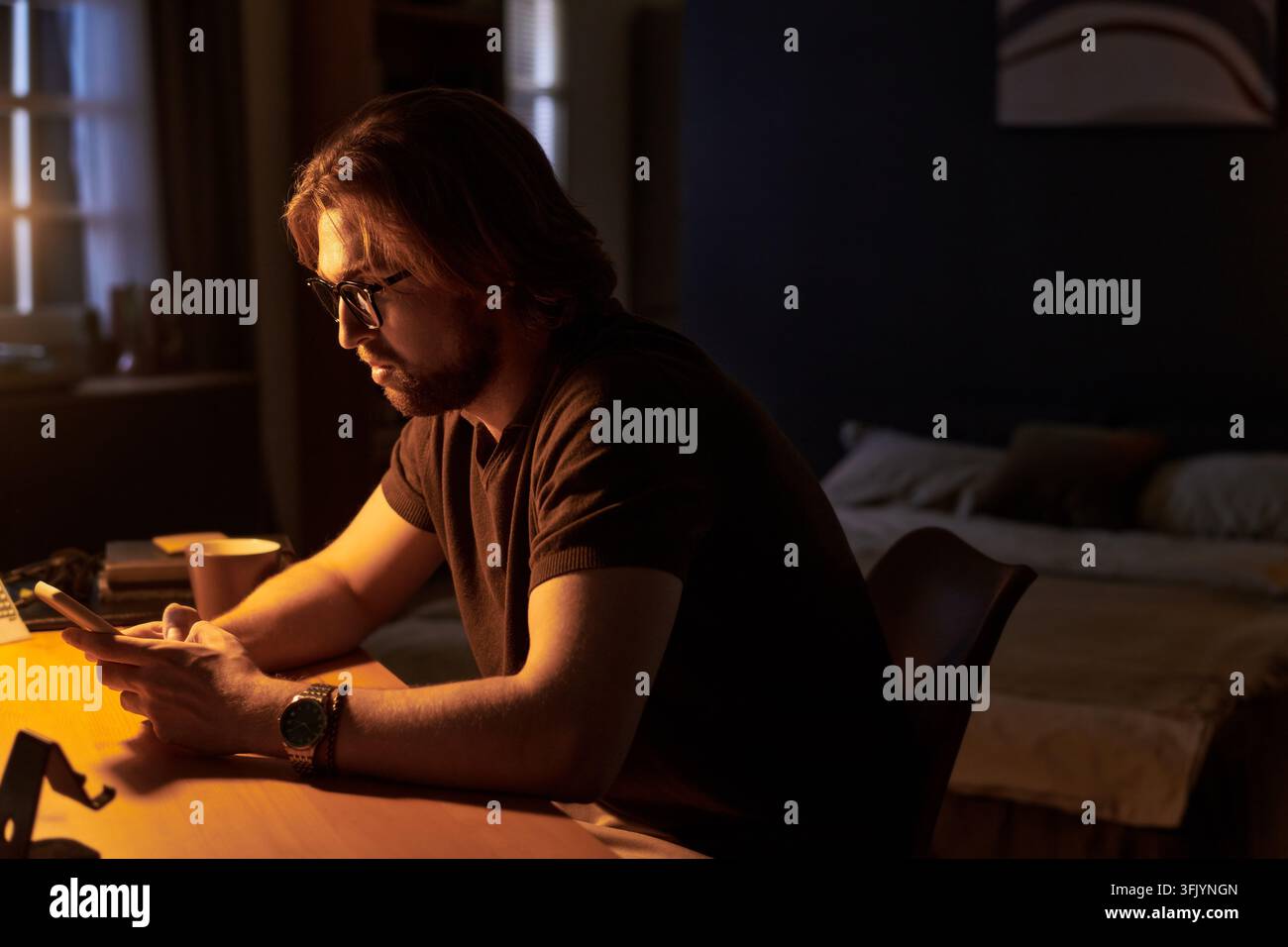 Uomo che usa uno smartphone seduto alla scrivania in una stanza buia di notte Foto Stock