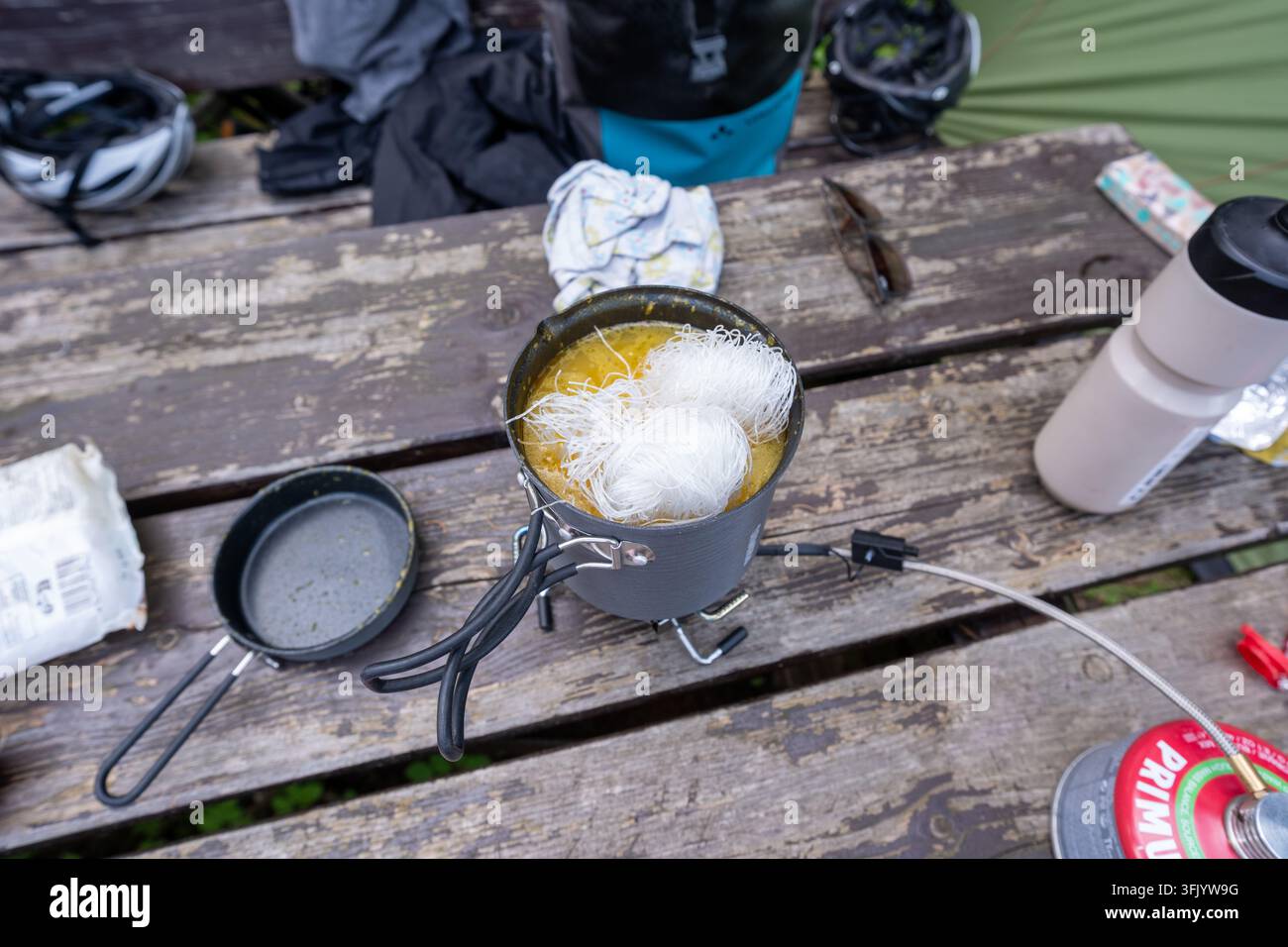 Preparazione del pasto in campeggio con noodles di riso in brodo giallo su una stufa compatta da backpacking, perfetta per i contenuti di avventura all'aperto e di viaggio. Foto Stock