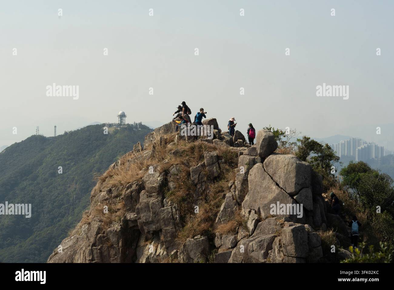 Gli escursionisti si riposano e visitano la cima del Lion Rock a Hong Kong, godendosi vedute panoramiche con l'iconica stazione radar sullo sfondo. Foto Stock