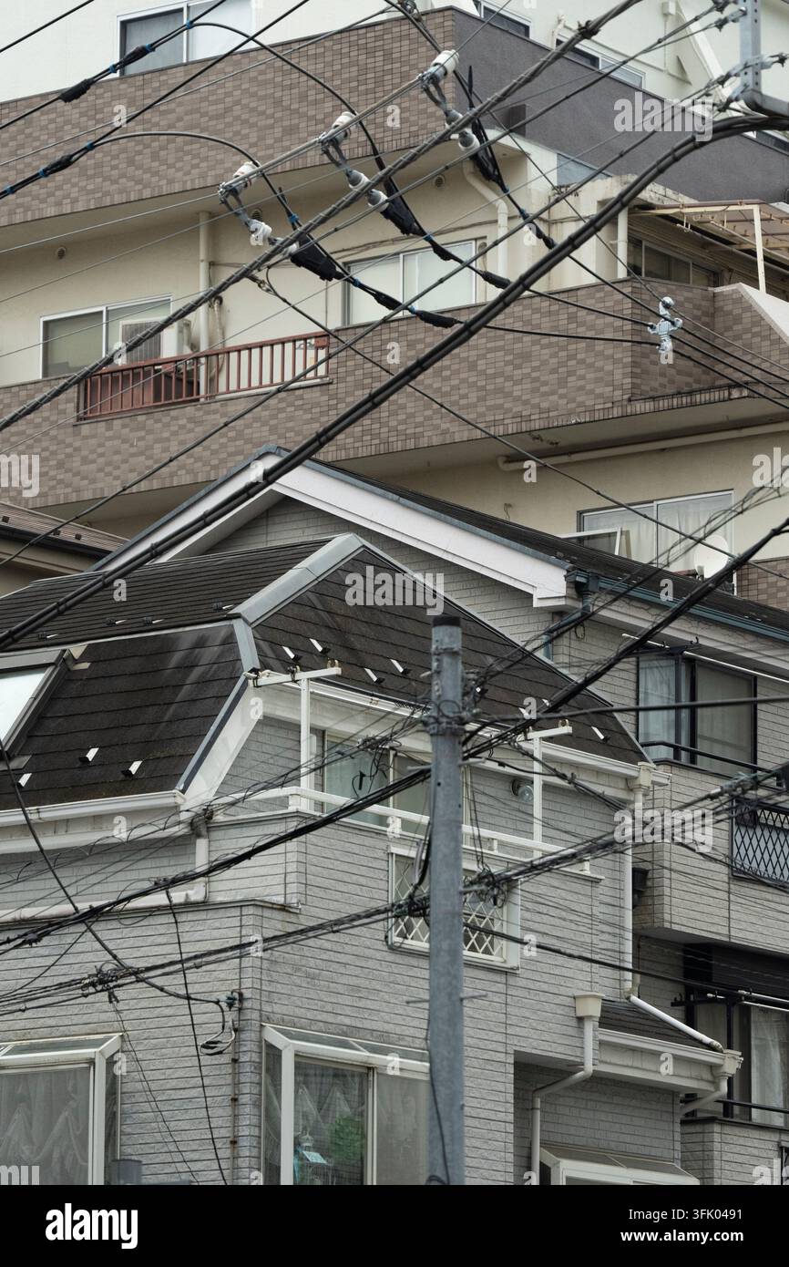 Una fitta rete di cavi di servizio sospesi si incrocia sui edifici residenziali a Tokyo, Giappone, per fornire servizi essenziali di energia elettrica e telecomunicazioni. Foto Stock